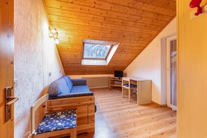 Une pièce mansardée chaleureuse, avec un plafond en pente, une lucarne, un canapé, un bureau et un ordinateur.