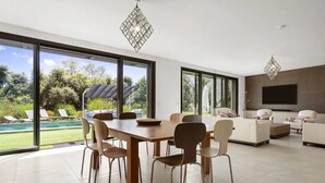 A modern living room with a dining area, large windows, and a pool view. - Holiday Home 'Rez De Villa Pour 8 Valeriane' with Shared Pool, Private Garden and Wi-Fi (Trans-en-Provence)