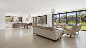 A spacious living area with a sofa, armchairs, and a dining table. Large windows provide a view of the outdoors. - Holiday Home 'Rez De Villa Pour 8 Valeriane' with Shared Pool, Private Garden and Wi-Fi (Trans-en-Provence)