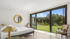 A bedroom with a bed, a chair, a table, a mirror, and a large sliding glass door leading to a garden. - Holiday Home 'Rez De Villa Pour 8 Valeriane' with Shared Pool, Private Garden and Wi-Fi (Trans-en-Provence)