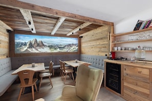 Una habitación acogedora con techo de madera, un ventanal con vistas a la montaña, una mesa de comedor con sillas y una estantería.