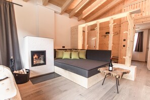 Tunnelmallinen huone, jossa on sohva, takka, pieni pöytä pullon kera ja puupalkit katossa.