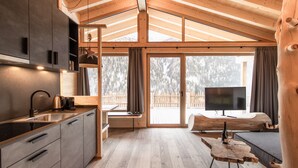 En modern stuga med ett kök, en matplats och ett stort fönster med utsikt över ett snötäckt landskap.