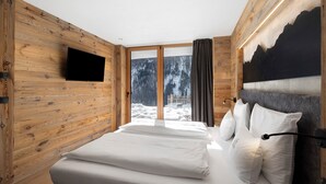A bedroom with a bed, a mounted TV, a large window with a view of a snowy landscape, and wooden walls.
