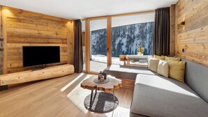 A modern living room with a flat-screen TV, wooden walls, a sofa, and a large window with a snowy view.