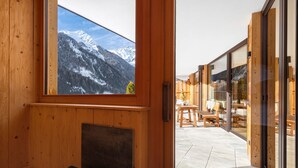 A wooden interior with a fireplace, a large window with a mountain view, and a glass door leading to an outdoor seating area.