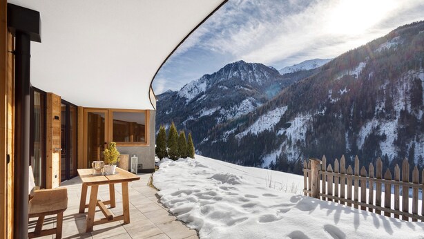 A wooden deck with a table and chairs, a wooden fence, and a view of snow-covered mountains.