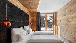 A bedroom with a wooden ceiling, a large bed with white bedding, and a view of a snowy landscape through a sliding door.
