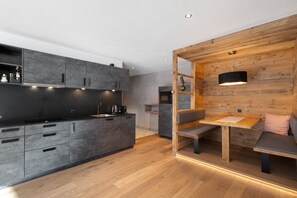 A modern kitchen with grey cabinets, a wooden dining area with a bench, and a pendant light.