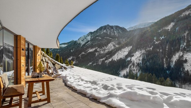 A terrace with a view of snow-covered mountains, wooden furniture, and a white canopy.