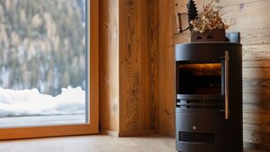 A wood-burning stove in a room with a wooden wall and a window overlooking a snowy landscape.