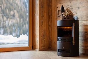 A wood-burning stove in a room with a wooden wall and a window overlooking a snowy landscape.