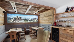 Um quarto aconchegante com teto de madeira, uma janela grande com vista para as montanhas, uma mesa de jantar com cadeiras e uma estante de livros.