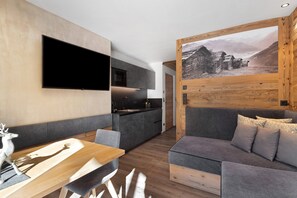 A modern living space with a kitchen, a dining area, and a large painting on the wall. - Holiday Apartment 'Chalet-Suite Wiese' with Mountain View, Private Terrace and Wi-Fi (Selva dei Molini)