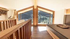 A room with a wooden staircase, a bed, and large windows offering a forest view.