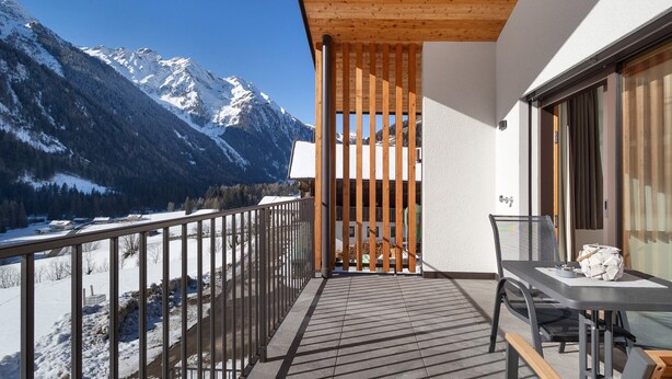 A balcony with a view of snow-covered mountains, a wooden ceiling, and a table with chairs.