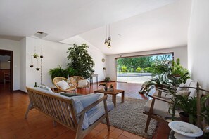 Un soggiorno spazioso con soffitto alto, mobili in legno e ampie finestre che offrono vista sull'esterno.