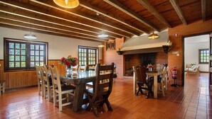 Uma ampla sala de jantar com mesas e cadeiras de madeira, janelas grandes e uma lareira de tijolos.