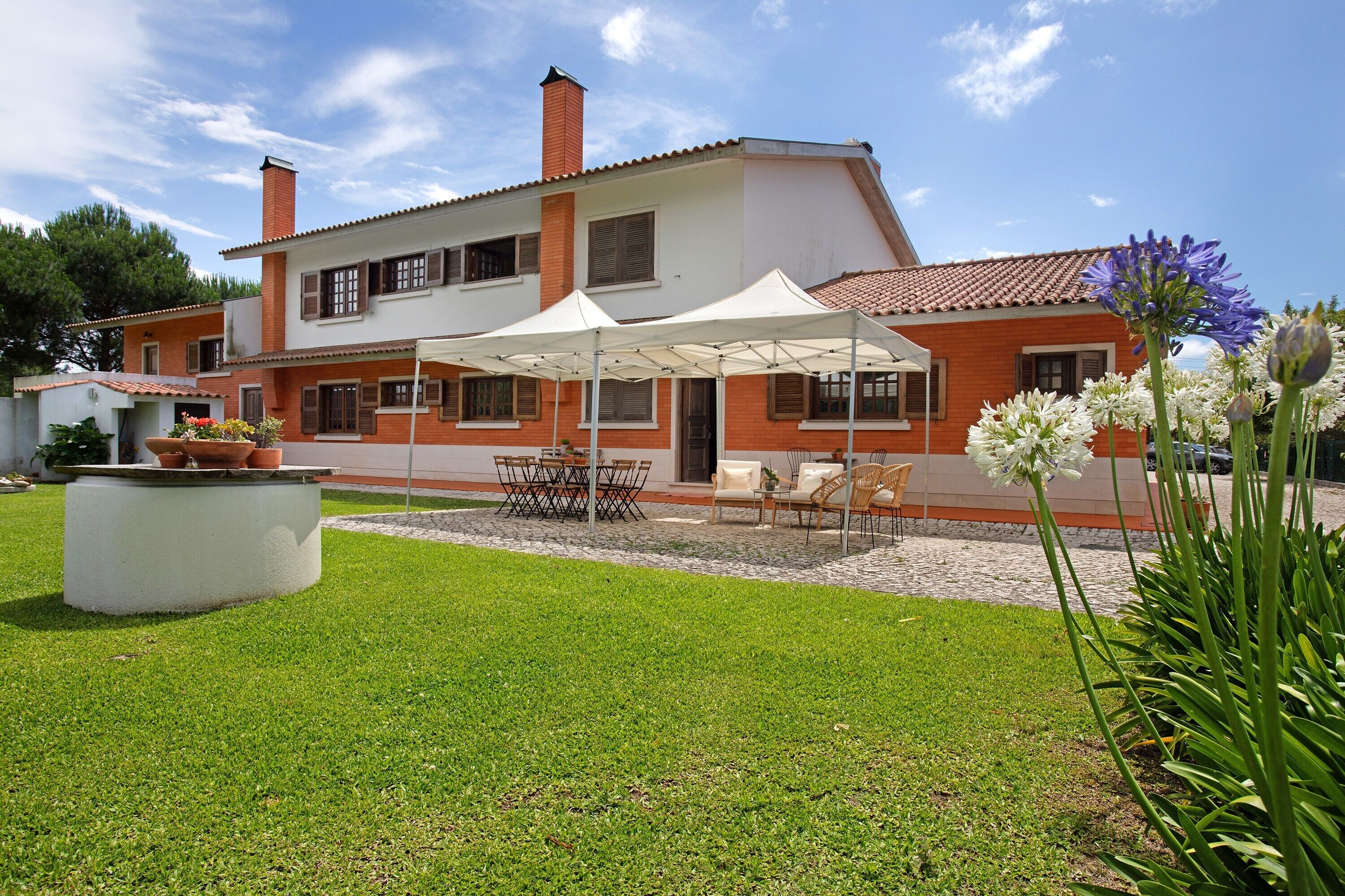 Una casa a due piani con patio, mobili da giardino e un giardino.
