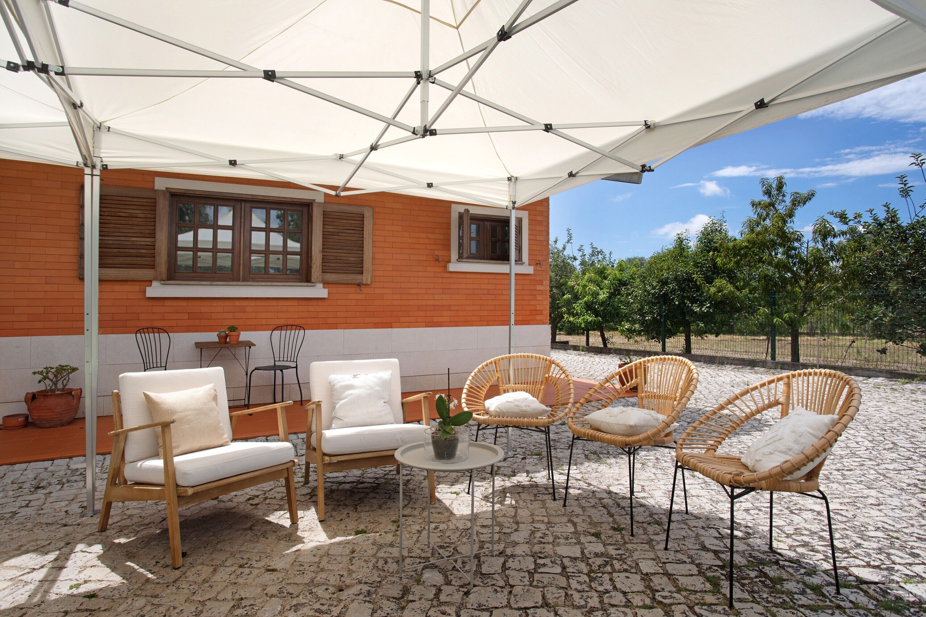 An outdoor patio with wicker furniture, a white umbrella, and a brick building with windows.