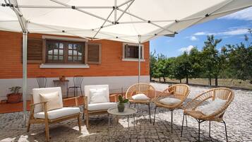An outdoor patio with wicker furniture, a white umbrella, and a brick building with windows.