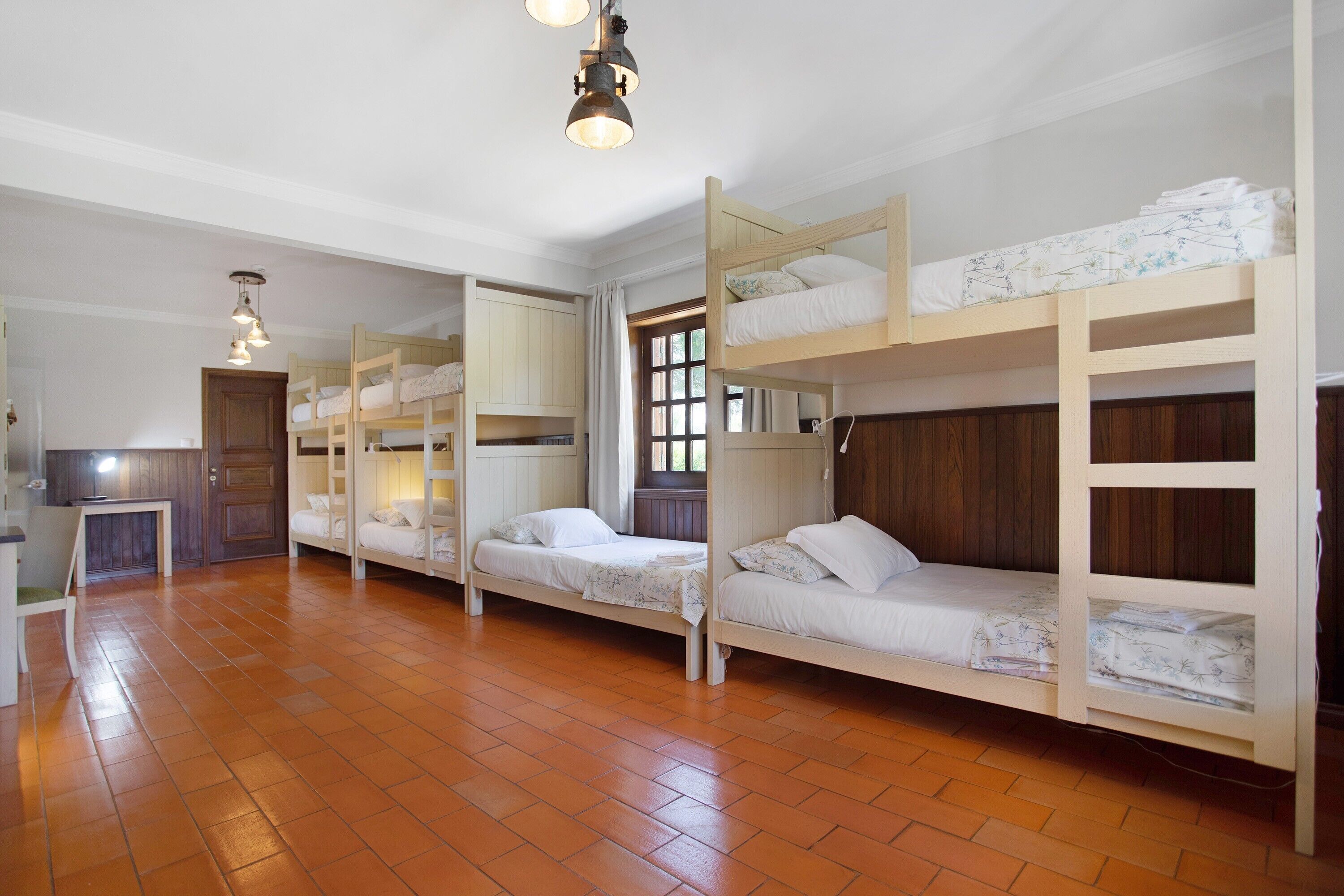 A room with bunk beds, a desk, and a window with curtains.