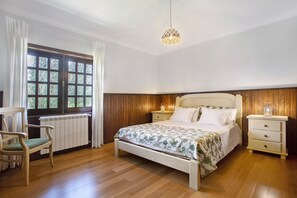 Una camera da letto con pavimento in legno, un letto con copripiumino floreale, un comodino con lampada, una sedia e una finestra con tende.