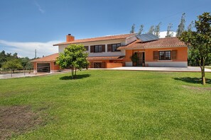 A two-story house with a tiled roof, a front lawn, and a small tree.