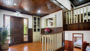 Um lobby com piso de madeira, uma escada, uma porta com placa de saída de emergência, um espelho e uma cama ao fundo.