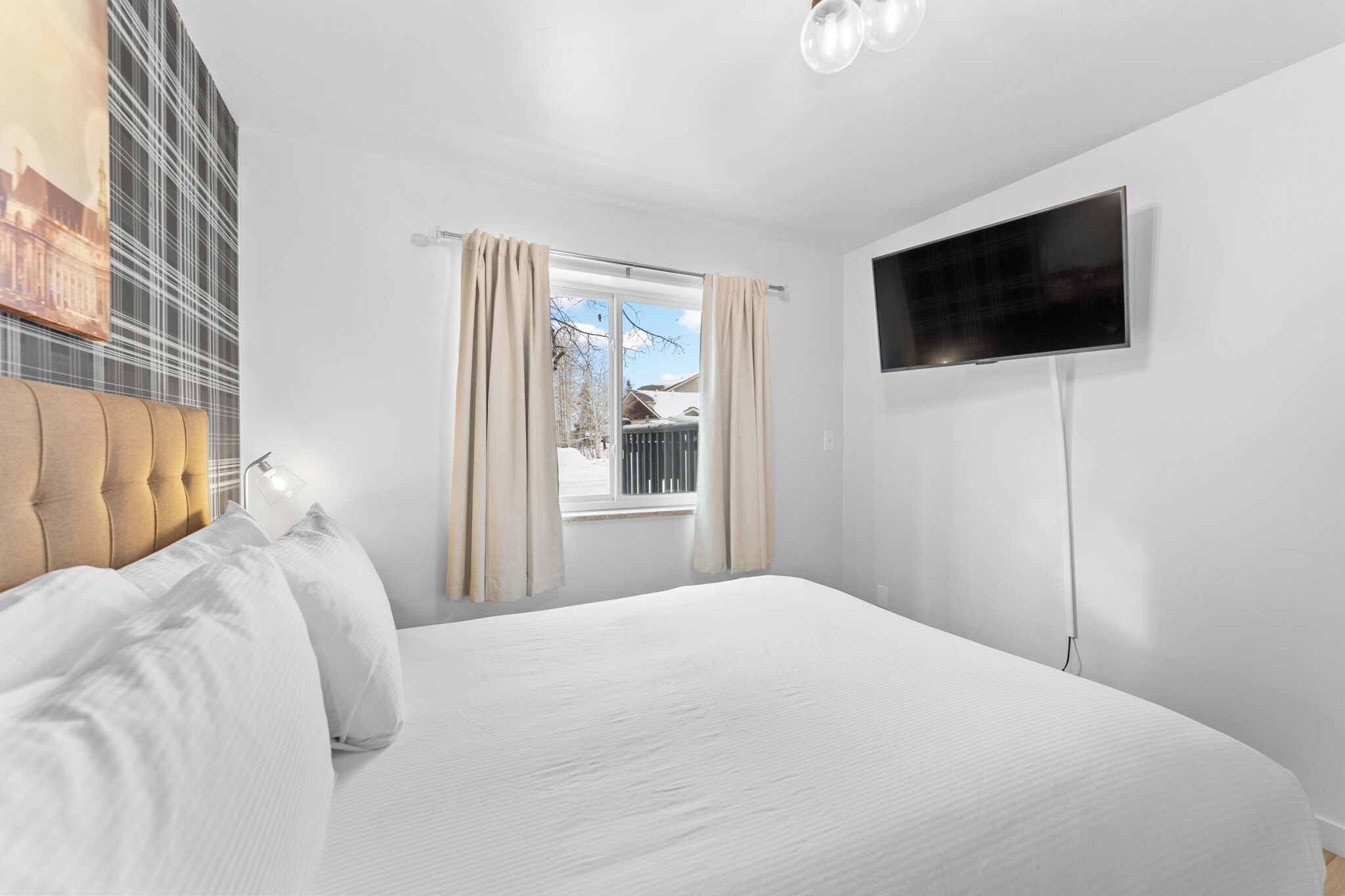 Quarto de hotel com uma cama grande, televisão de tela plana na parede e uma janela com cortinas.