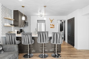 A modern kitchen with a central island, bar stools, and a hanging light fixture.