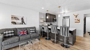 Ein modernes Wohnzimmer mit grauem Sofa, einem Couchtisch und einer Küchenzeile mit Barhocker.