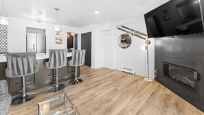 Ein modernes Wohnzimmer mit Kamin, zwei Barhocker, einem Fernseher und einem runden Spiegel.