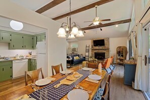 A spacious dining area with a long wooden table set for four, a kitchen with green cabinets, and a living room with a fireplace. - Cozy Family Cabin • Steps to Lake • Canoe • Firepit • Pet Friendly (Pocono Lake)