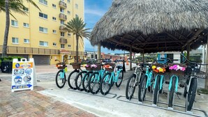 Um hotel na praia com estrutura de telhado de palha, bicicletas com cestas e um aviso de aluguel.