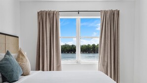 Quarto com uma grande janela, uma cama e vista para a água e árvores.