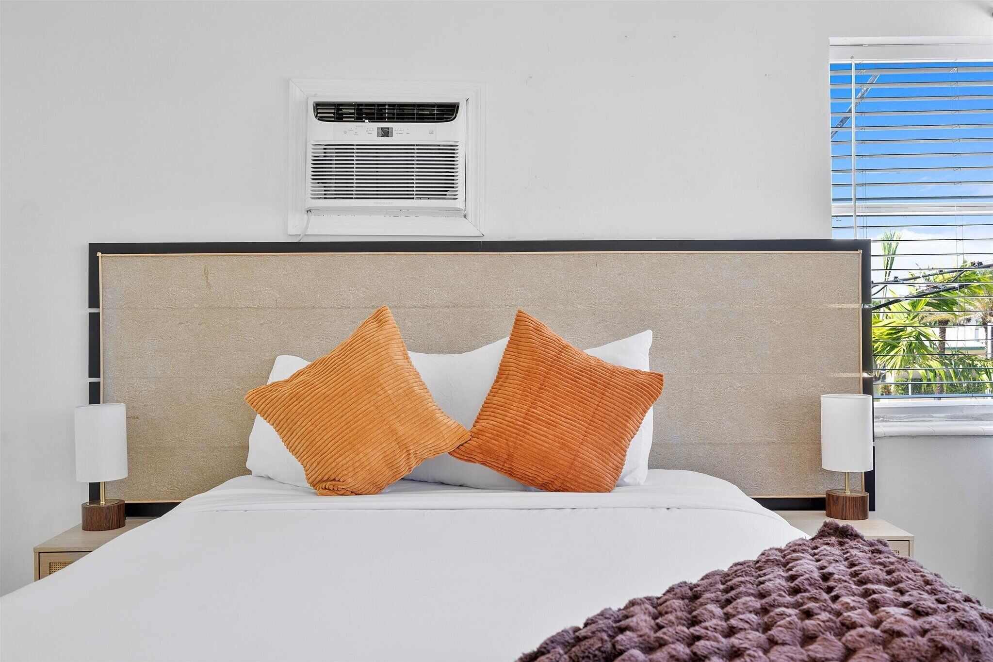 A neatly made bed with two orange pillows, a white headboard, and a small bedside table with a lamp.