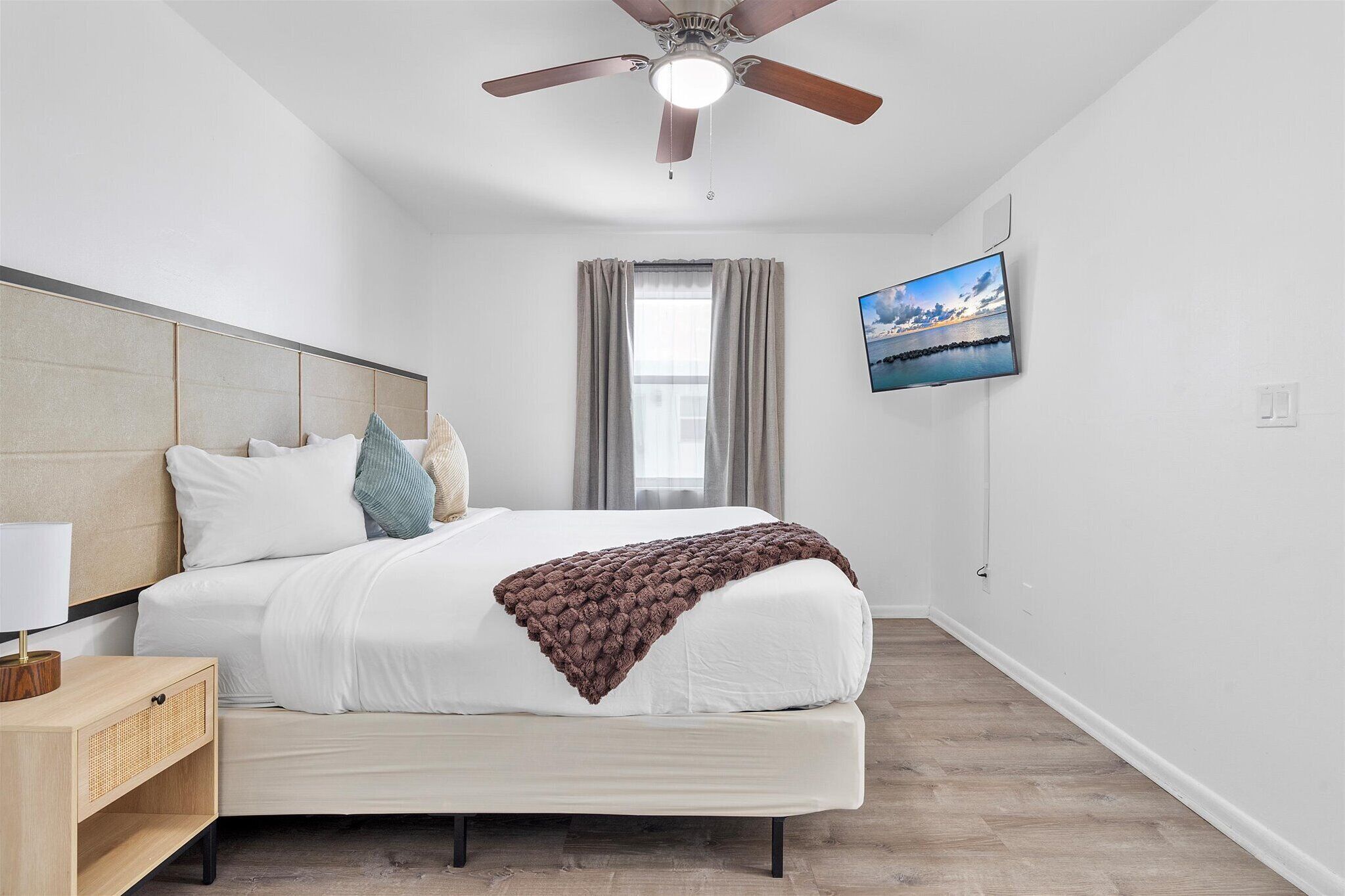 A bedroom with a bed, a nightstand, a ceiling fan, a TV, and a window with curtains.
