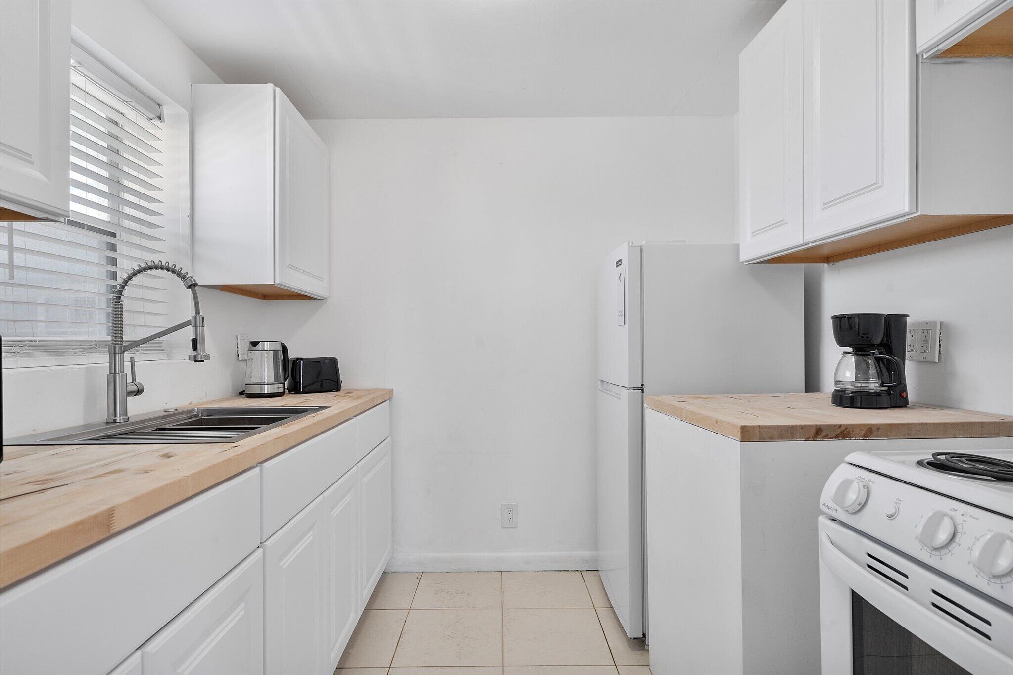 A modern kitchen with white cabinets, a stainless steel sink, a coffee maker, a refrigerator, and a gas stove.