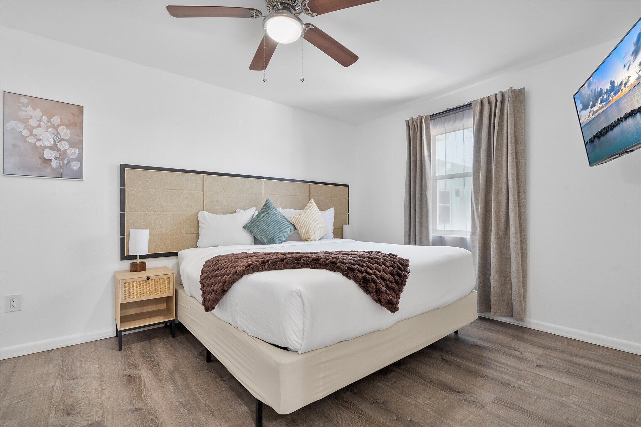 Een slaapkamer met een bed, nachtkastje, plafondventilator en een raam met gordijnen.