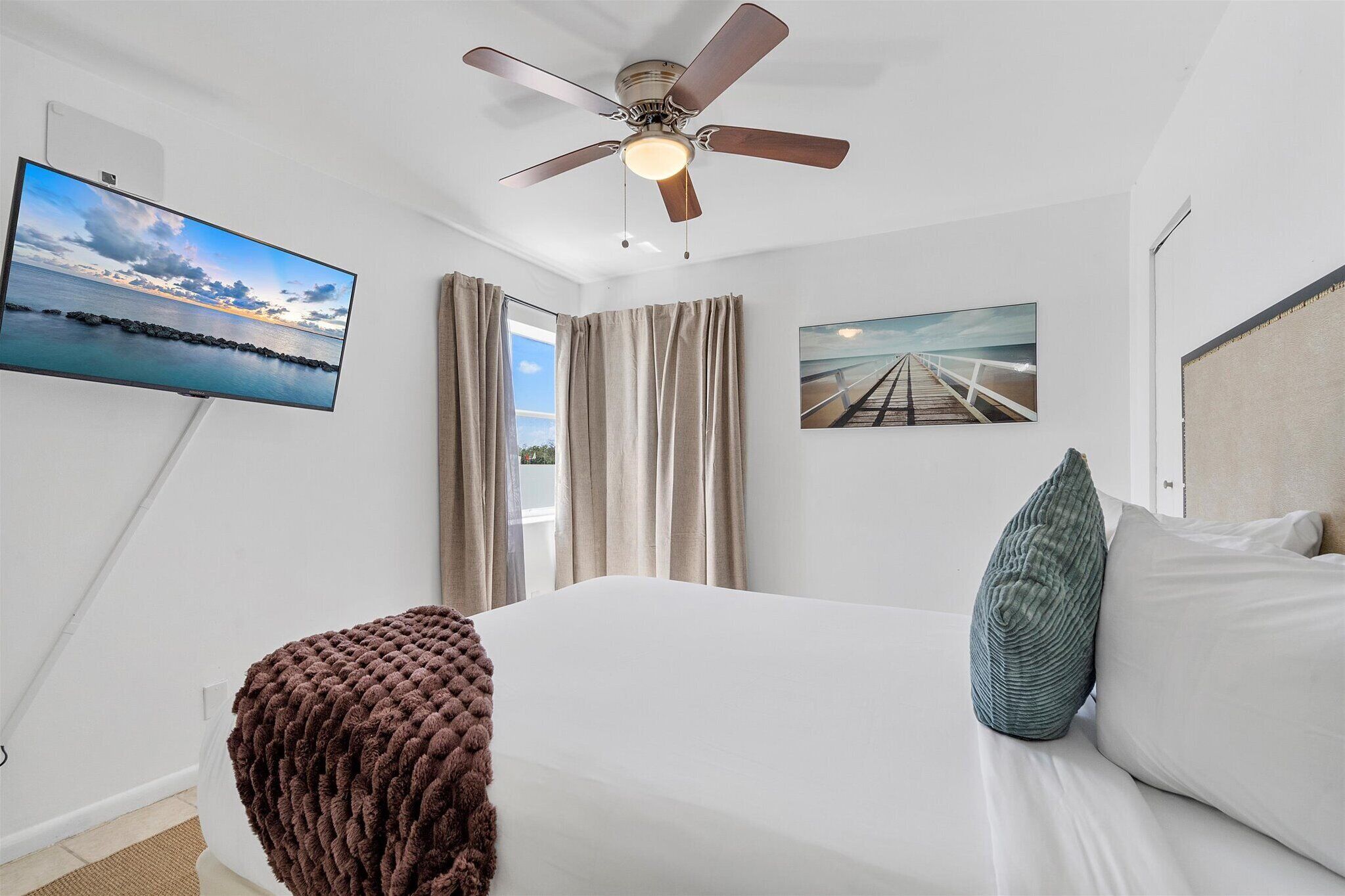 A bedroom with a bed, a ceiling fan, a TV, and a painting.