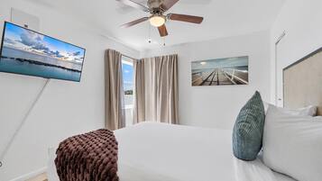 A bedroom with a bed, a ceiling fan, a TV, and a painting.