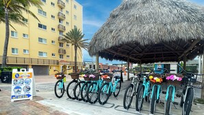A beachfront hotel with a thatched-roof structure, bicycles with baskets, and a rental sign. - Coastal Sunset (Hollywood)