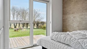 A bedroom with a large sliding glass door leading to an outdoor area with a wooden deck and a view of trees and a grassy field. - Cozy home in Haderslev with WiFi (Haderslev)