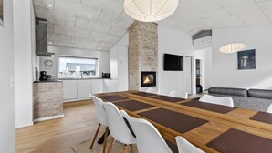 A modern kitchen with a large window, a fireplace, and a dining area with a long table and chairs. - Cozy home in Haderslev with WiFi (Haderslev)