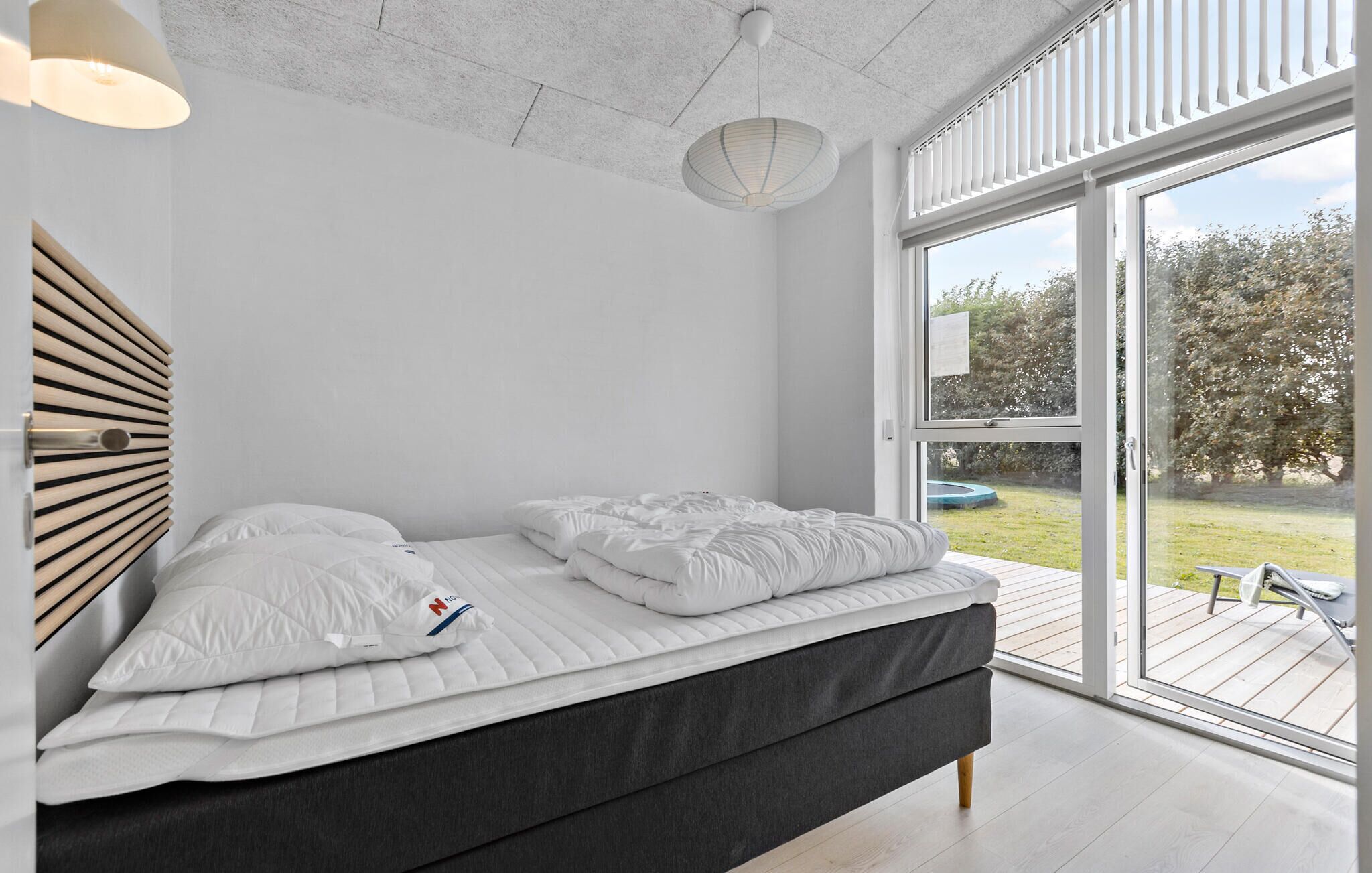 A modern bedroom with a large bed, a ceiling light, and a view of the outdoors.