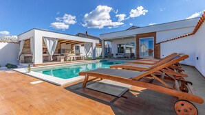 Un espace piscine extérieur moderne, doté de chaises longues, d’un barbecue et d’un coin salon abrité.