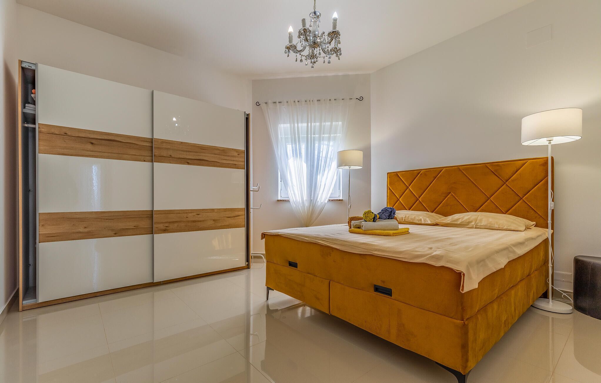 A bedroom with a bed, a wardrobe, a chandelier, and a floor lamp.