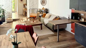 A spacious living area with a wooden floor, a sofa, a dining table, and a kitchen area with cabinets. - Maison Plein Centre, Idéale Pour un Couple (Pont-l'Abbé)