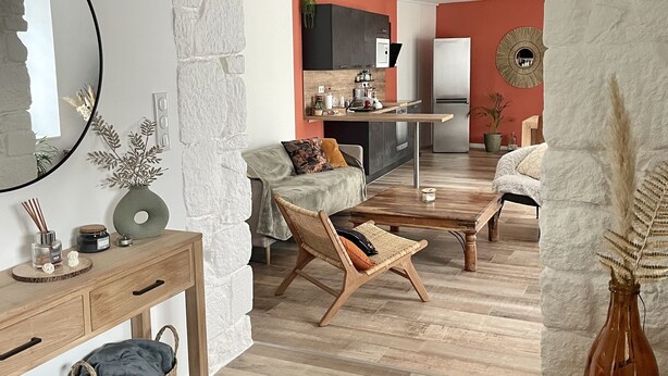A cozy living room with a wooden coffee table, a wicker chair, and a sofa. A kitchen is visible in the background with modern appliances. - Maison Plein Centre, Idéale Pour un Couple (Pont-l'Abbé)